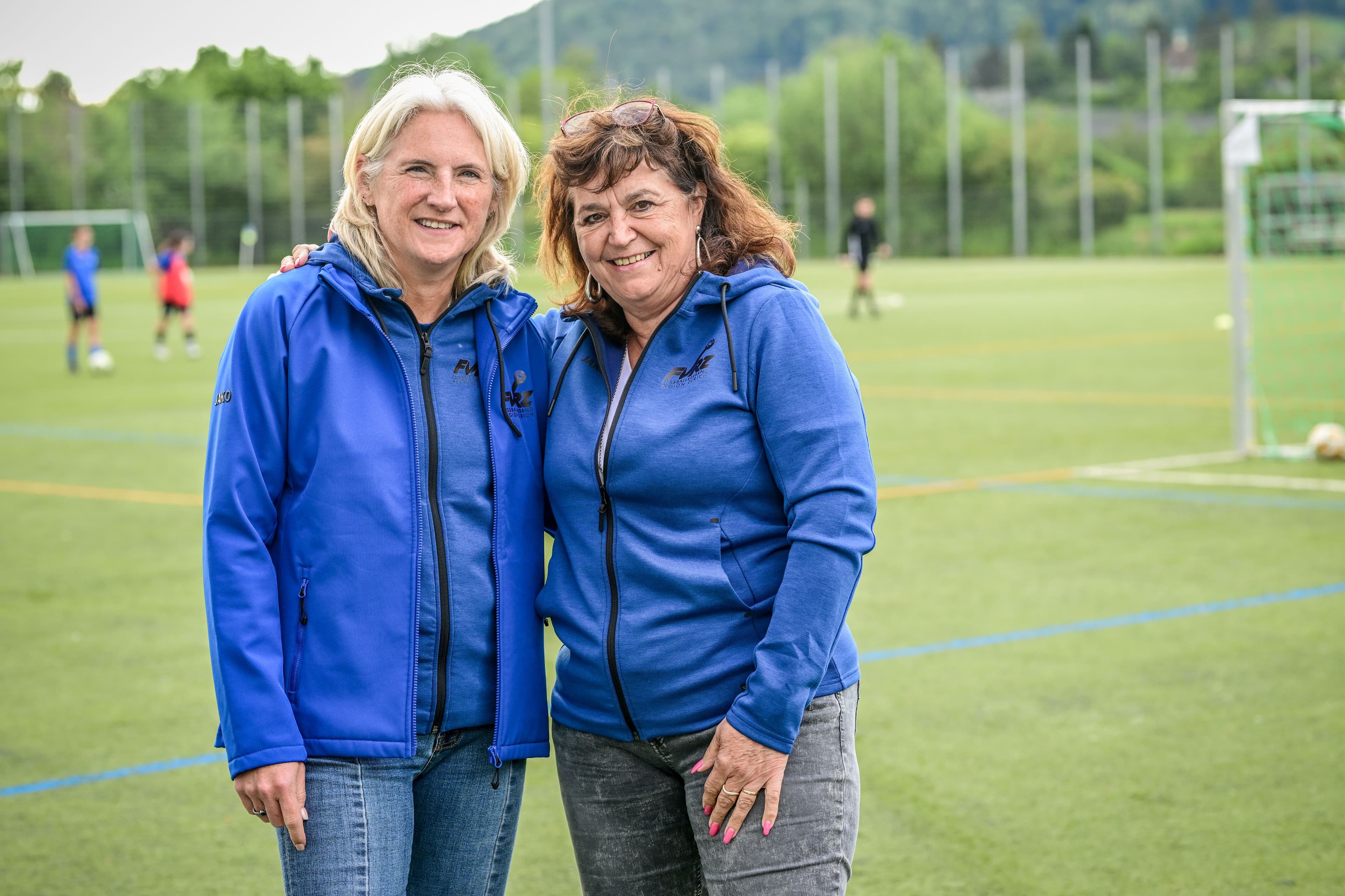 Claudia Feller und Rita Zbinden stehen auf dem Fussballplatz und schauen in die Kamera. 